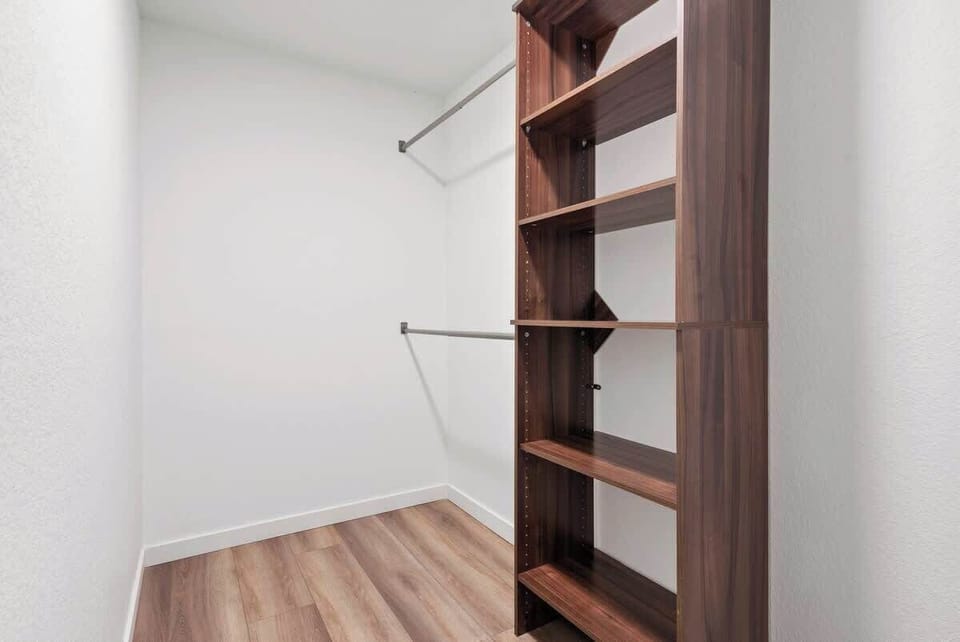 Spacious walk-in closet with sleek wooden shelves and hanging rods. Features modern design, ample storage, and light wood flooring for organized and easy access to your belongings.