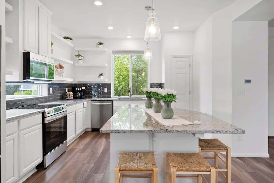 Bright kitchen with granite island, stainless steel appliances, and white cabinetry. Open layout with natural light and cozy seating. Ideal for cooking and relaxing. Book now for a stylish and comfortable stay!