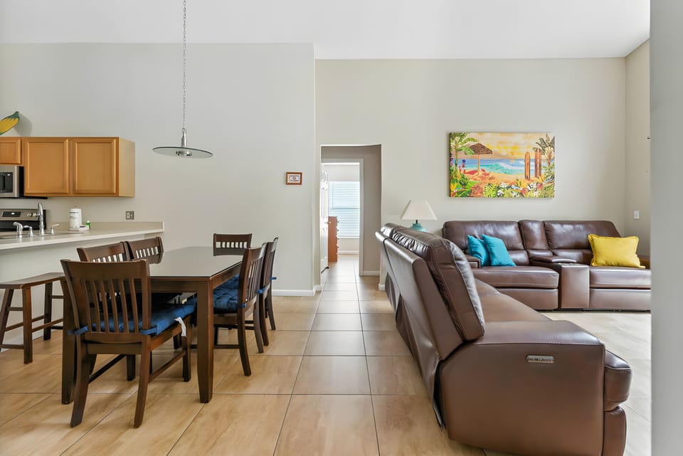 Enjoy the warm natural light in this spacious living area with rich leather sofas and colorful pillows. The charming wooden dining table invites you to share meals and create lasting connections with loved ones.