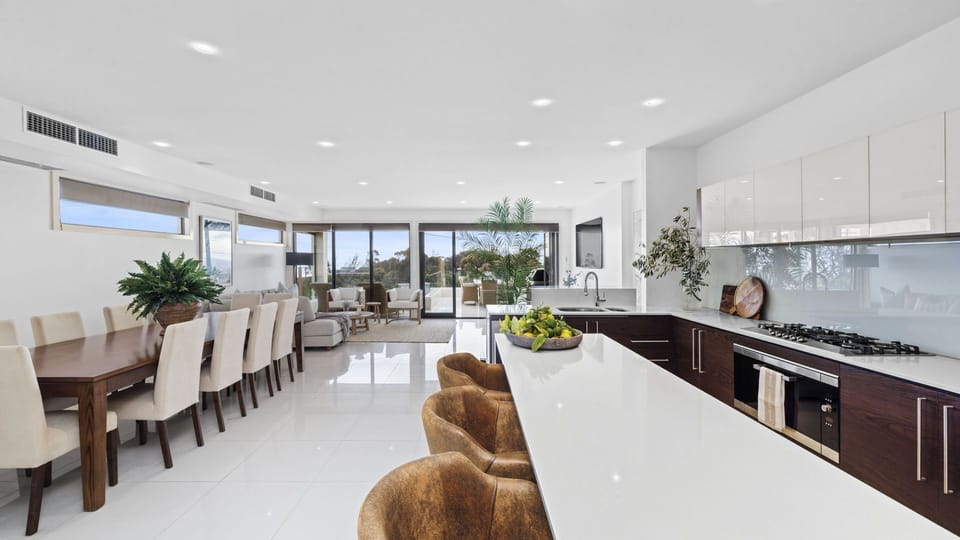 Open plan living area with L-shaped couch, Smart TV, and coffee table, with large Bi-fold patio doors that open on to the tiled terrace,