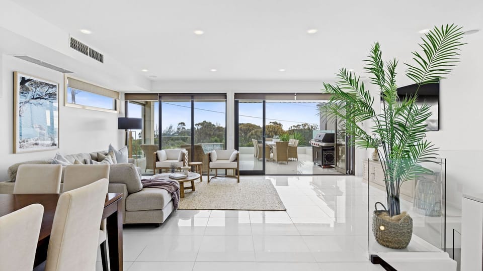 Bright and coastal, the upstairs open-plan living and dining area combines cosy comfort with style, slide open the doors to let the ocean breeze in, or gather for meals with bay glimpses in the background.