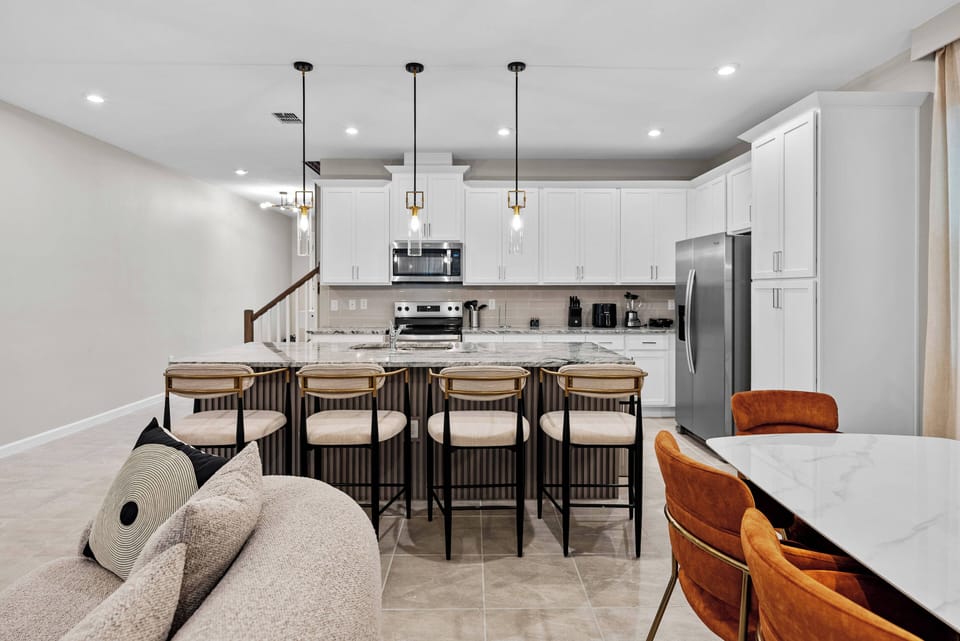 Welcome to this stylish kitchen, featuring sleek white cabinetry and a spacious stone-topped island. The modern pendant lighting creates a warm atmosphere, perfect for memorable meals and gatherings with your loved ones.