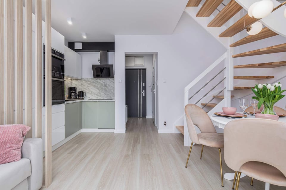 A wider perspective of the living room combined with a functional kitchenette. A wooden staircase leads from the living room to the bedroom.