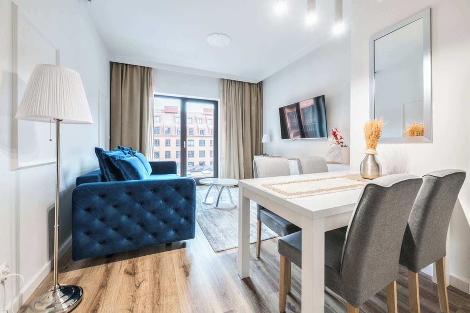 A dining table with chairs is positioned near a blue sofa, creating a cohesive living and dining area.  The room is well-lit and appears to be part of a larger space.