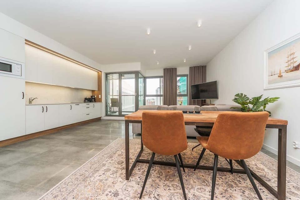 The centerpiece is a chic wooden coffee table with a geometric pattern, adding character to the room. A modern flat-screen TV in the corner is ideal for evening entertainment.