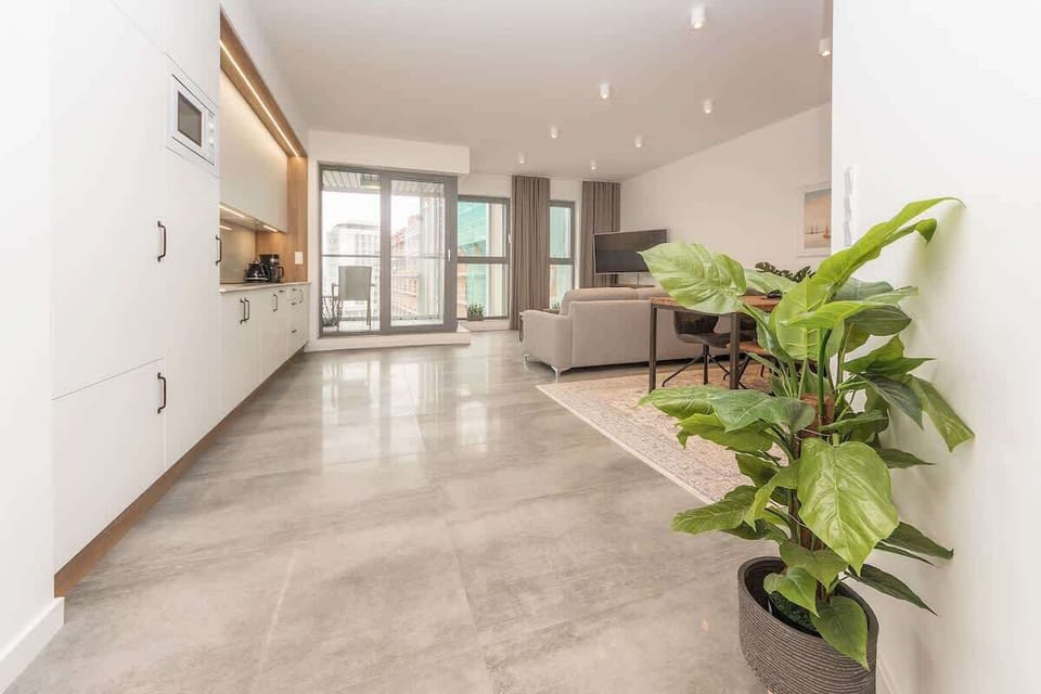Large panoramic windows fill the space with natural light and offer a picturesque view of the surrounding cityscape. The centerpiece is a chic wooden coffee table with a geometric pattern, adding character to the room. A modern flat-screen TV in the 