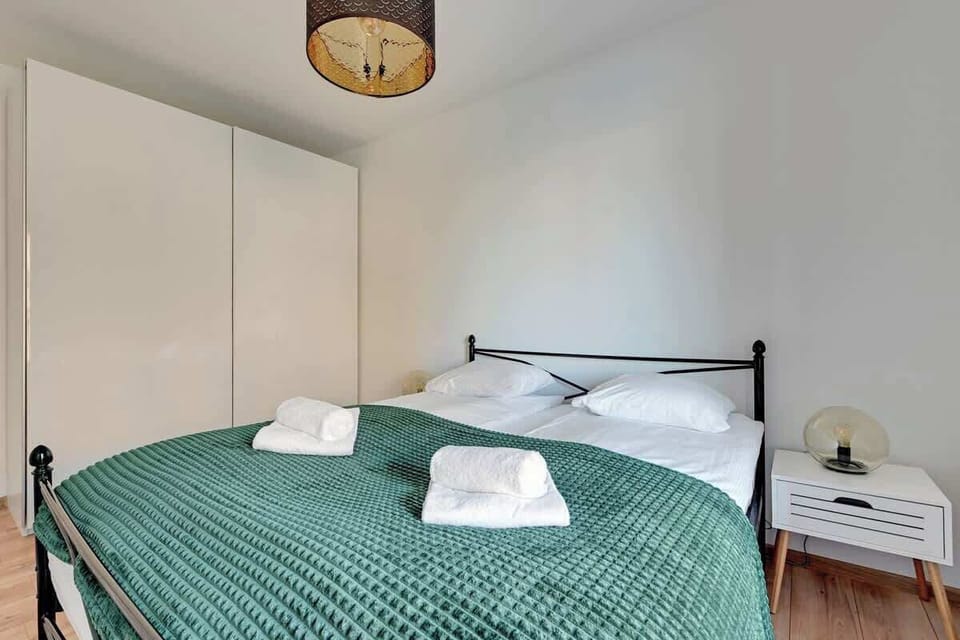 A cozy bedroom featuring a double bed with green bedding, wooden flooring, and a bright ambiance.