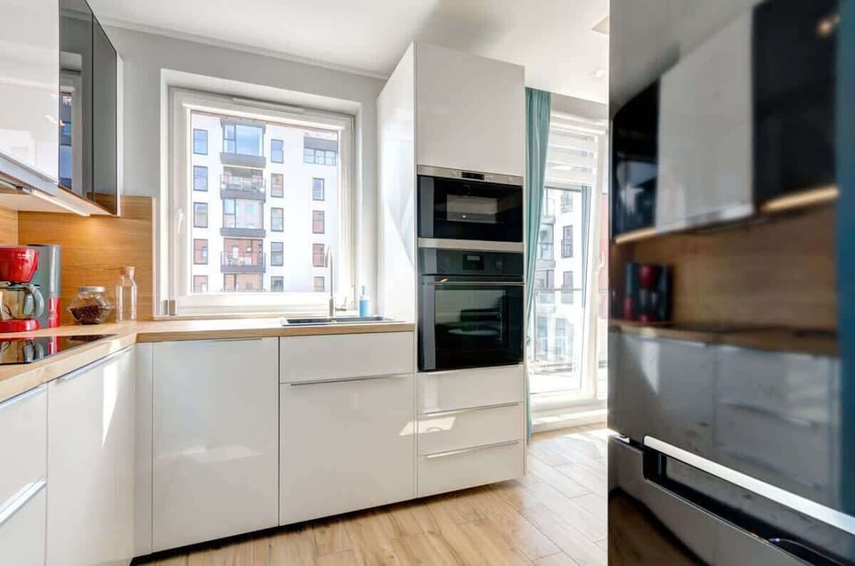 The modern kitchen in a light-colored interior with a wooden countertop, perfectly illuminated by a large window and equipped with high-quality appliances, combines minimalist style with full functionality.