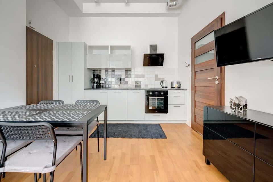 A modern kitchenette with light furniture and dark details seamlessly connects with the living room, creating a minimalist and functional space with a warm character.