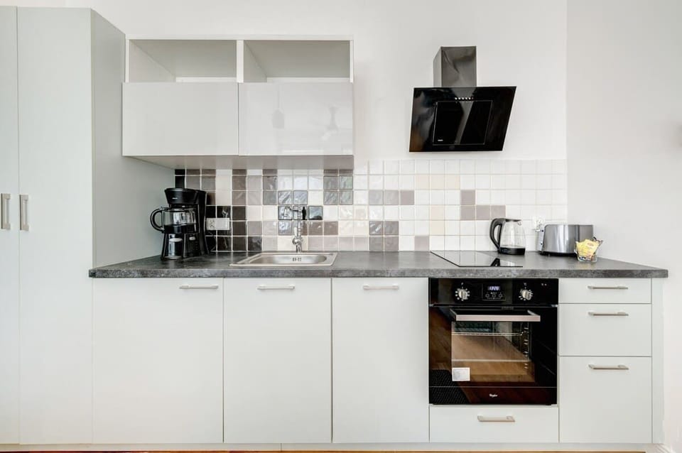 A modernly equipped kitchenette in light colors with a contrasting countertop and a subtle mosaic on the wall combines simplicity with functionality.