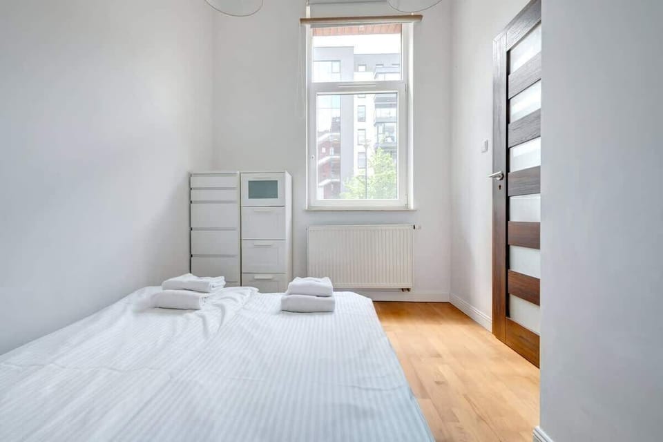 A bright, minimalist bedroom with white furniture and a large window, creating a space full of light and peace.