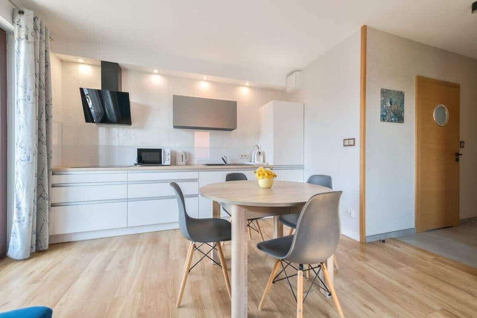 Airy, and contemporary, featuring sleek white cabinetry, modern appliances, and a minimalist dining area that promotes a clean, functional atmosphere.