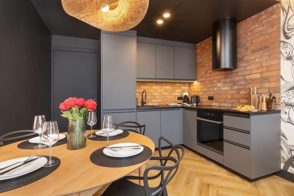 A stylish kitchen and dining area with dark cabinetry, brick walls, and modern lighting.

