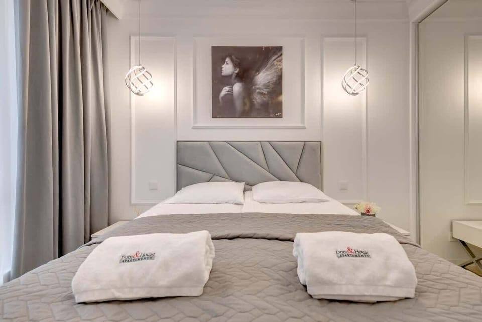 A neatly made bed with a geometric-patterned grey headboard, flanked by modern pendant lights and a stylish monochromatic portrait above, creating a sophisticated bedroom atmosphere.