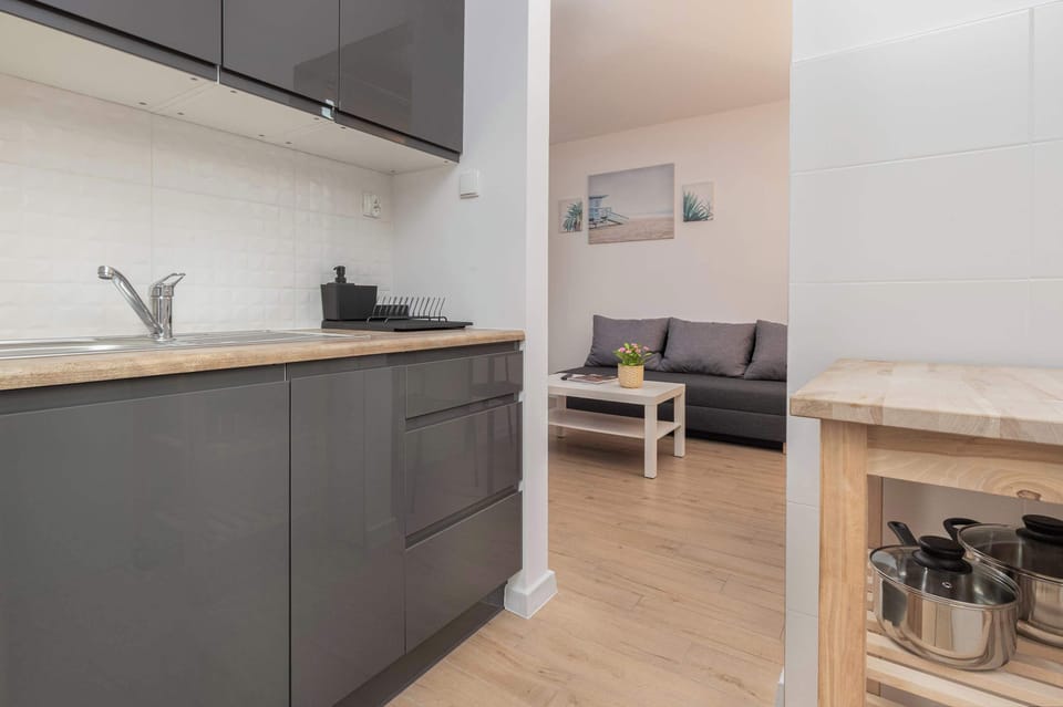 A modern kitchen with white and grey finishes, equipped with a dining table and visible appliances like a stovetop and oven. The design is simple yet functional.