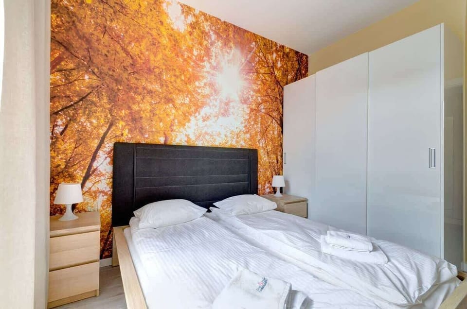 The bedroom features a striking autumn-themed wall mural, a comfortable bed with white linens, and a modern wardrobe.