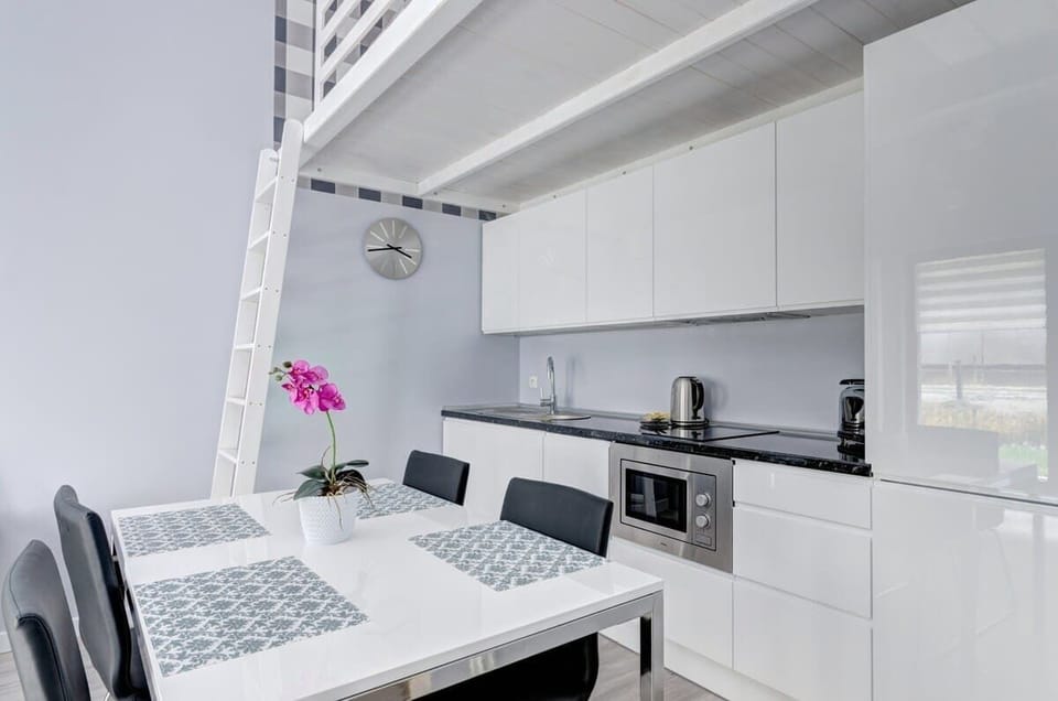 A modern kitchen with white cabinets, a black countertop, a dining table with decorative placemats, and a bright pink orchid as a centerpiece.