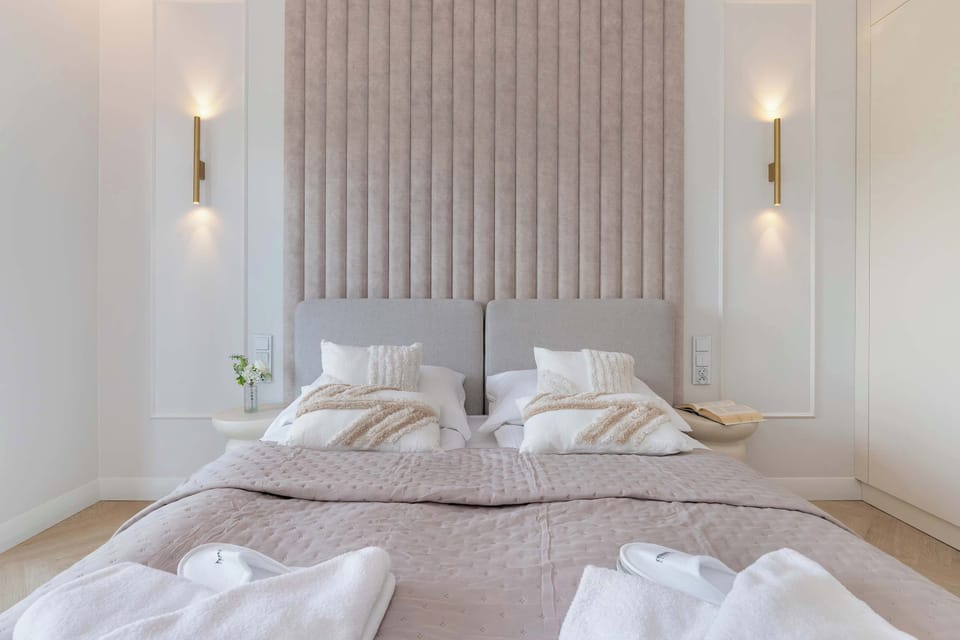 A cozy and elegant bedroom featuring a large double bed with a soft beige headboard and ambient lighting. Minimalist decor creates a calm and relaxing atmosphere.