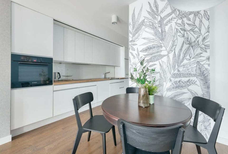 A spacious living area with a comfortable sofa, stylish armchairs, and a large window opening onto a balcony. The modern decor is accented with light tones and subtle decorative pieces.