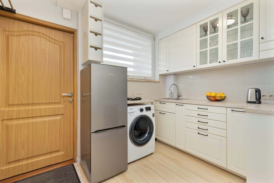 A wooden door next to the kitchen space with the washing machine and counter visible along one side.


