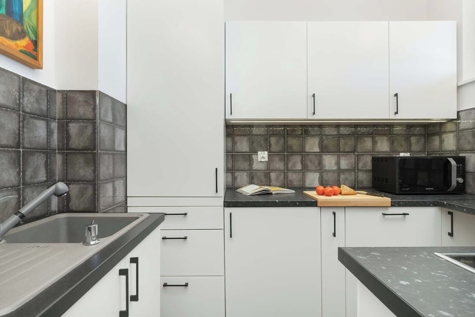 Modern kitchen with white cabinets and black handles, black countertop and gray tiles on the wall.