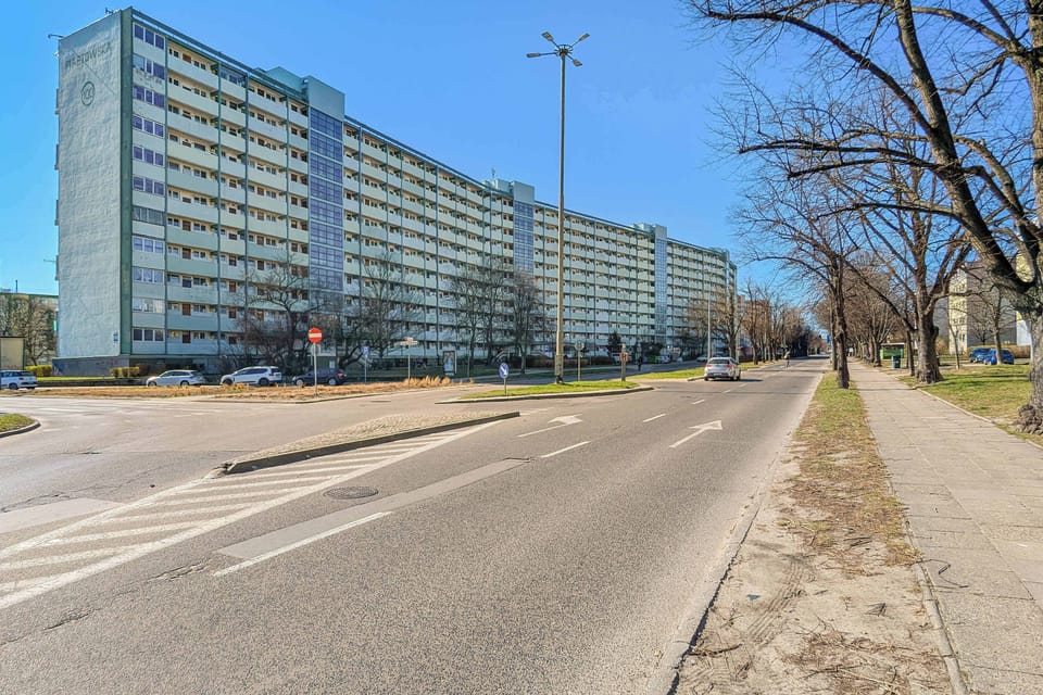 A multi-story, long residential building with numerous windows and balconies, located along the street.