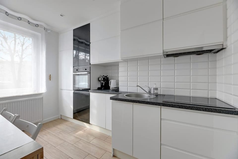 A charming dining space connected to a functional kitchen. The white dining table with wooden details and comfortable chairs invite guests to enjoy meals together.
