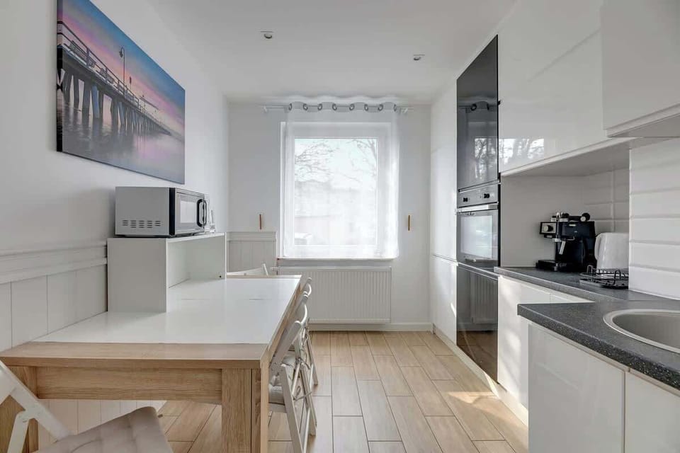 On the wall, there is a beautiful painting in pastel shades depicting a pier, which highlights the apartment's nautical style. The bright, elegant interior, filled with natural light, creates a cozy and harmonious atmosphere.