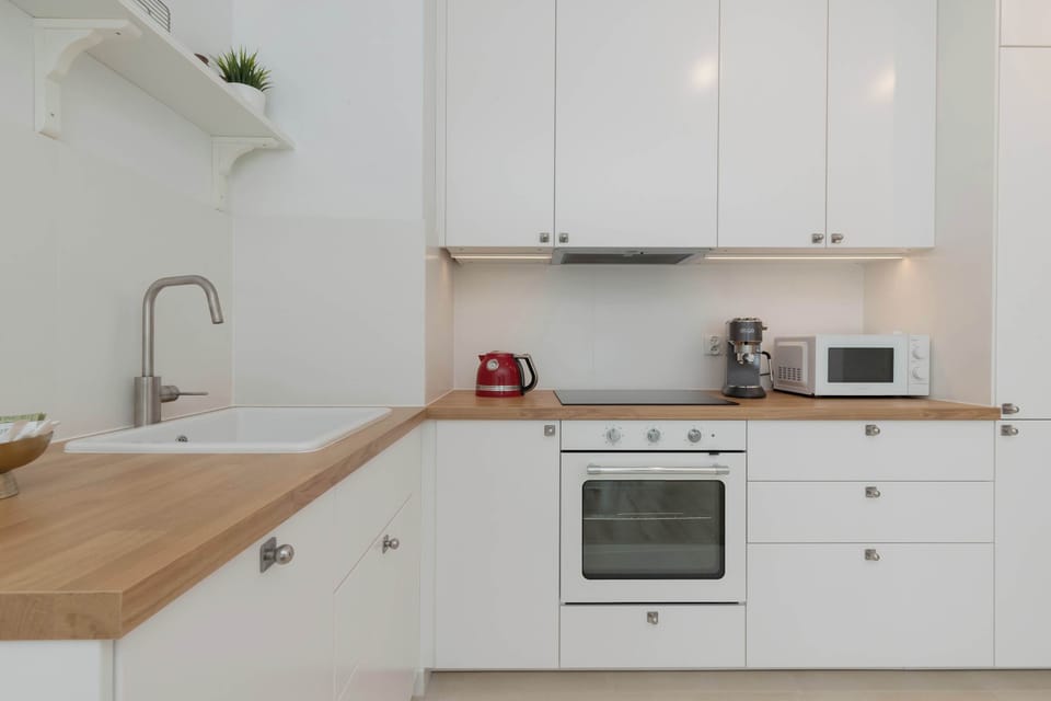A clean, white kitchen with built-in appliances and wooden countertop.