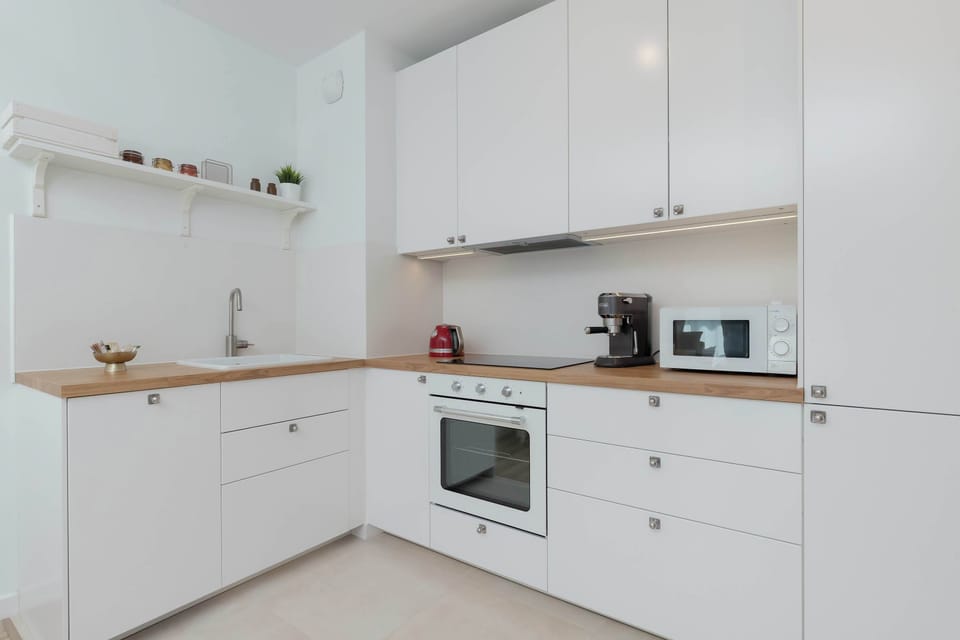 A clean, white kitchen with built-in appliances and wooden countertop.