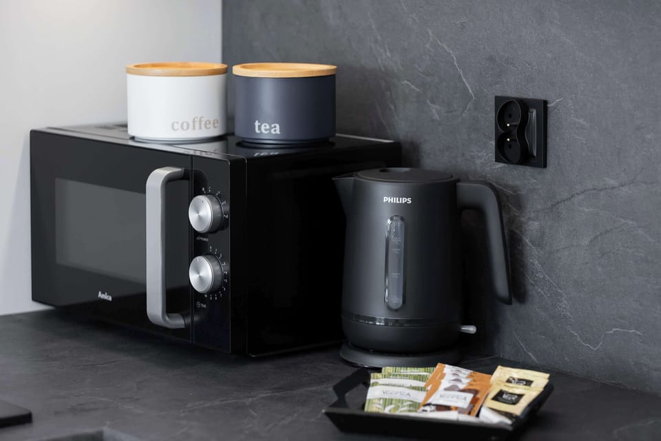 Discover a convenient corner, featuring a microwave, an electric kettle, and stylish containers for coffee and tea, inviting you to easily prepare your favorite hot beverages.