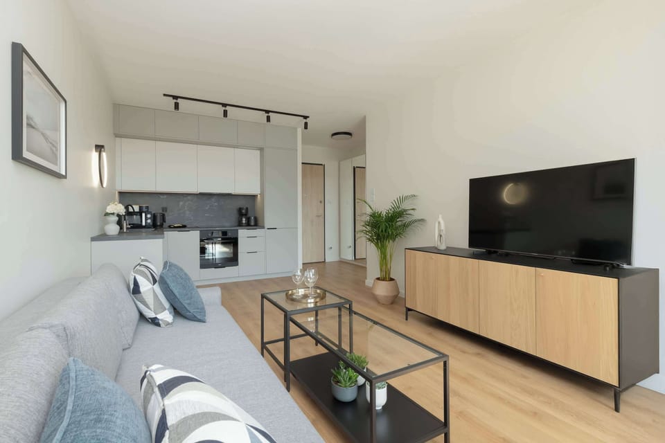 A spacious living room with a sectional sofa, wooden floors, a TV unit, and decorative plants adding a fresh touch.