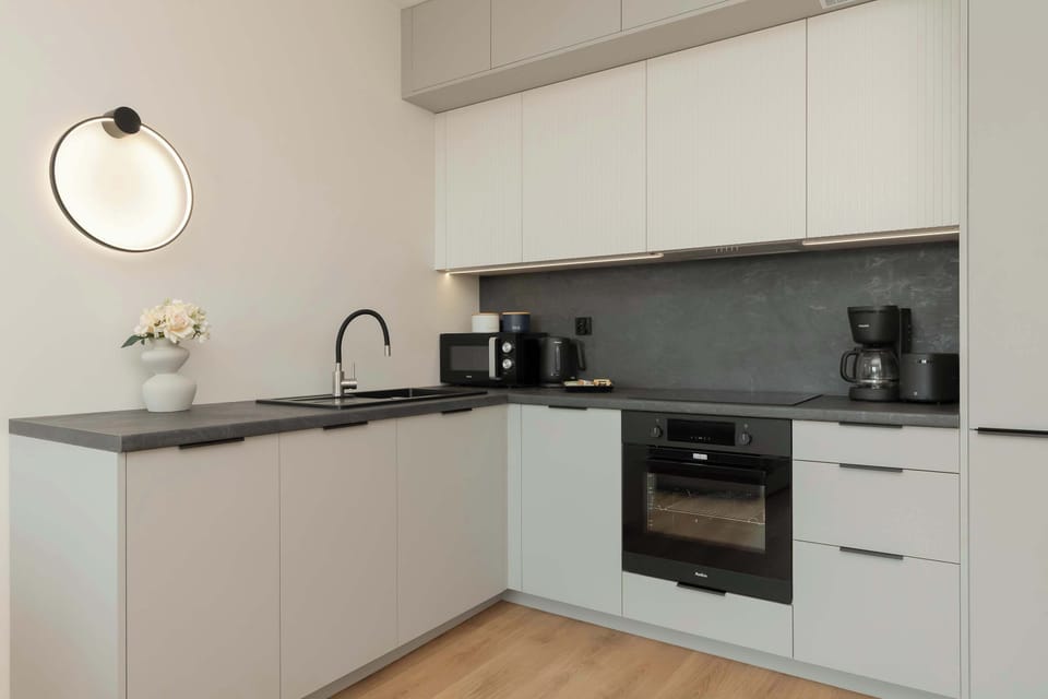 A modern kitchen setup with sleek white cabinetry, black countertops, and full appliances including an oven and coffee maker.