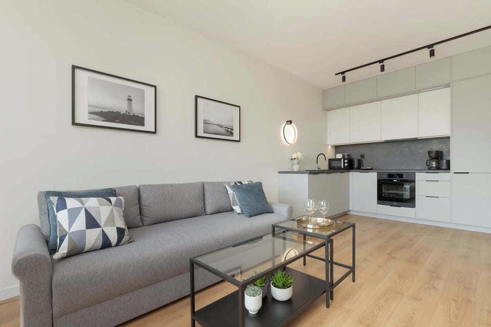 A cozy and elegant living space with a light gray sofa, a gold-accented coffee table, and a well-equipped kitchen area visible in the background.