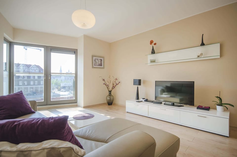 A bright sunny living room with a welcoming, warm atmosphere. A soft sofa and flat eran TV provide space to relax and unwind.