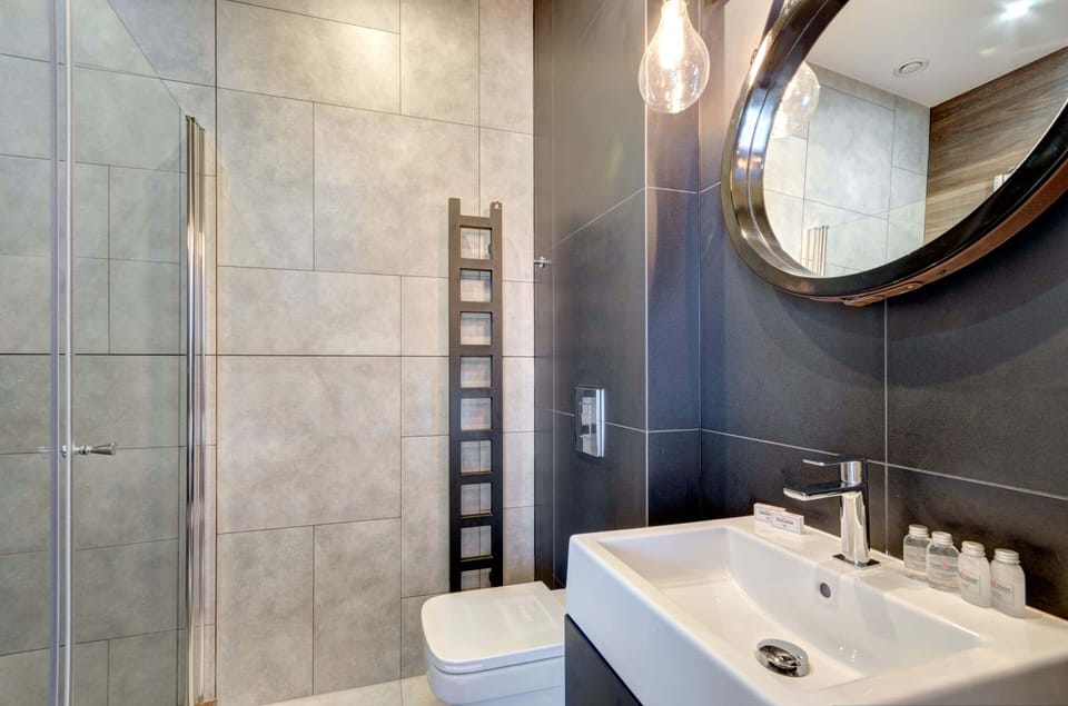 A modern bathroom with gray tiles, a circular mirror, and elegant fixtures.