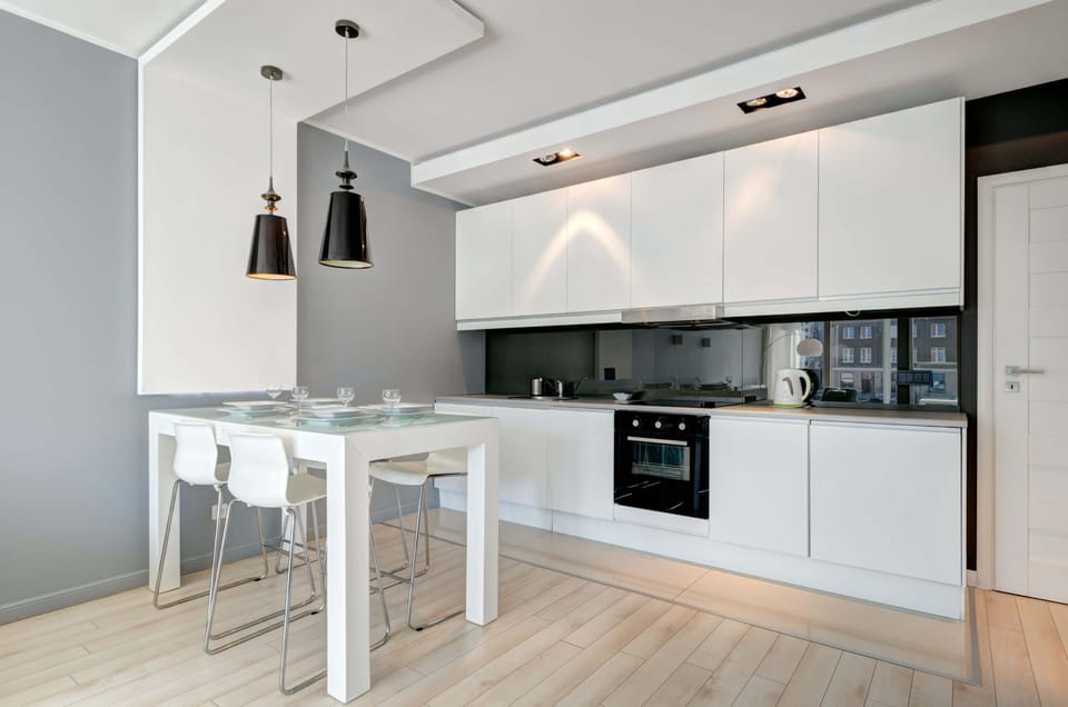 A modern kitchen with white cabinets, a sleek countertop, and black pendant lights. A stylish and functional space for cooking and dining.