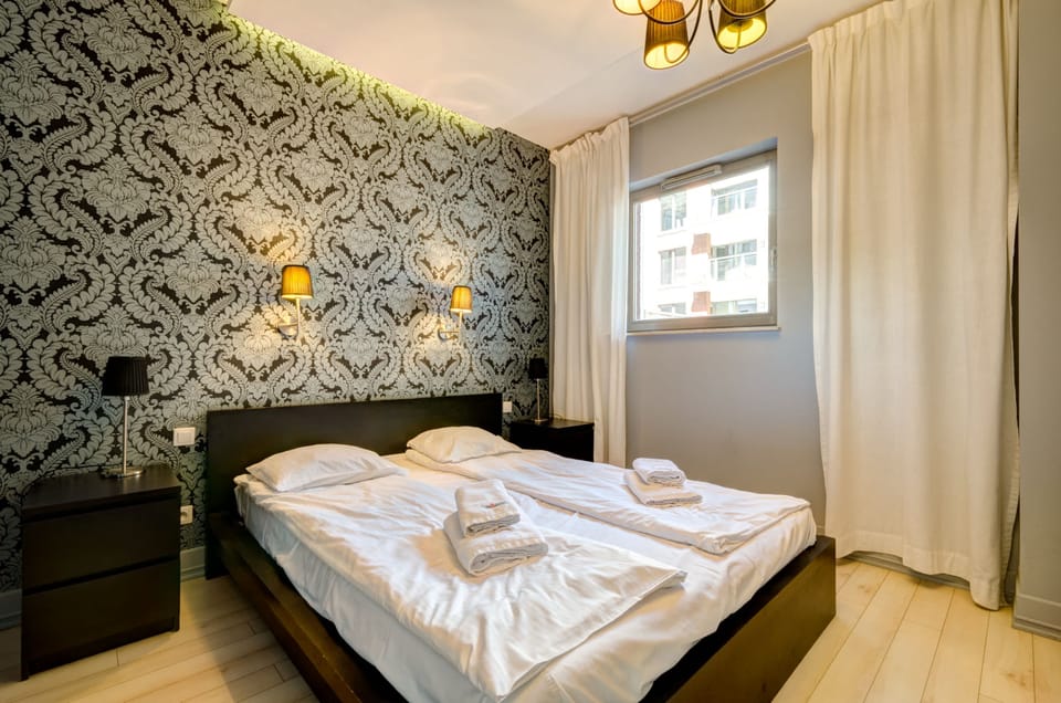 A cozy bedroom with a soft bed and artistic wallpaper on the feature wall. Ideal for a comfortable and stylish stay.