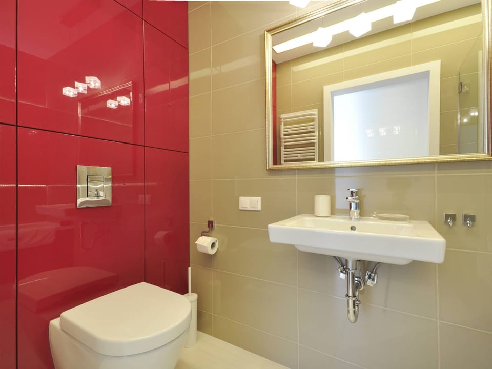 The thoughtfully designed bathroom combines simplicity with elegance. Bold red accents on one wall add character, while the bathtub with shower functionality and modern fixtures ensure comfort and convenience.