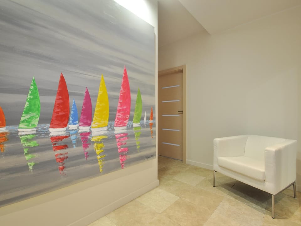 The hallway welcomes guests with a modern style and spaciousness. Bright walls and an elegant tiled floor visually enlarge the space, while a vibrant painting of colorful sailboats adds energy to the room. 