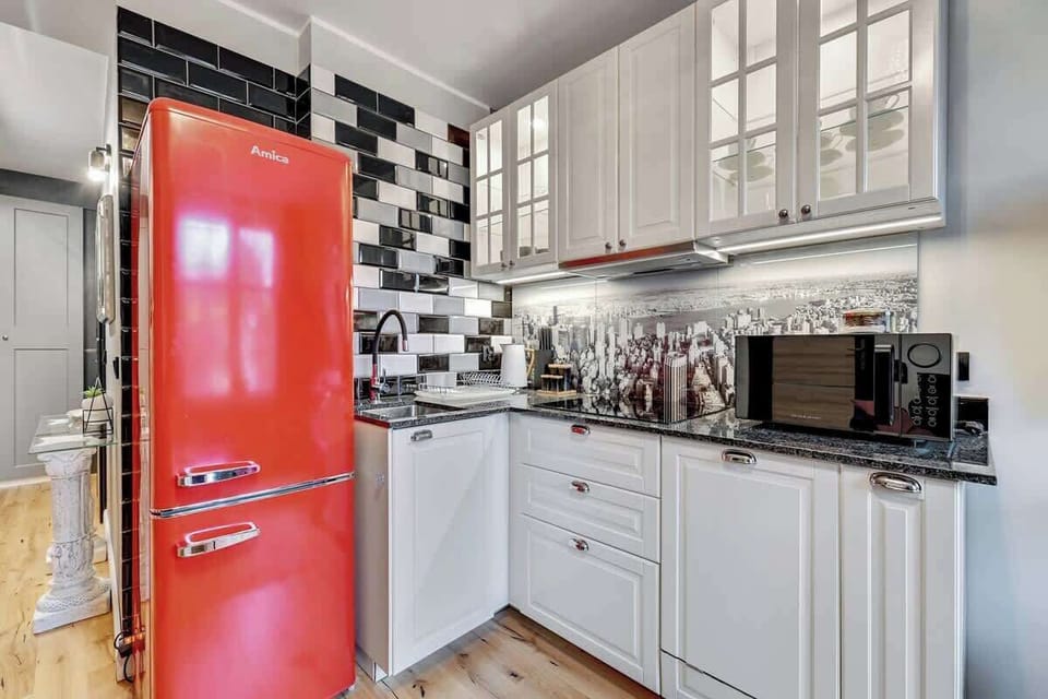  Glossy white cabinets contrast beautifully with the dark countertop, creating a striking visual balance. A retro-style refrigerator in a bold color adds character to the space, while a hob, oven and dishwasher ensure convenience when preparing meal.