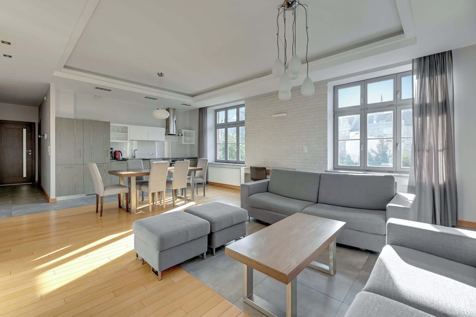A contemporary living space with a gray sectional sofa, a flat-screen TV, and views of greenery through the windows.