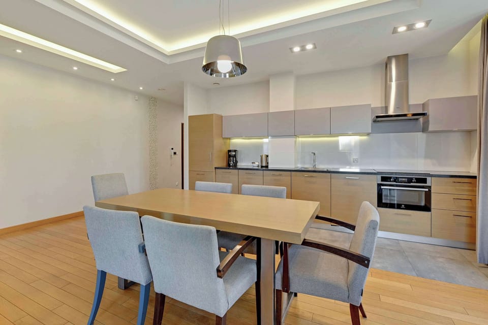 A spacious dining setup with a wooden table and upholstered chairs, surrounded by natural light from large windows.