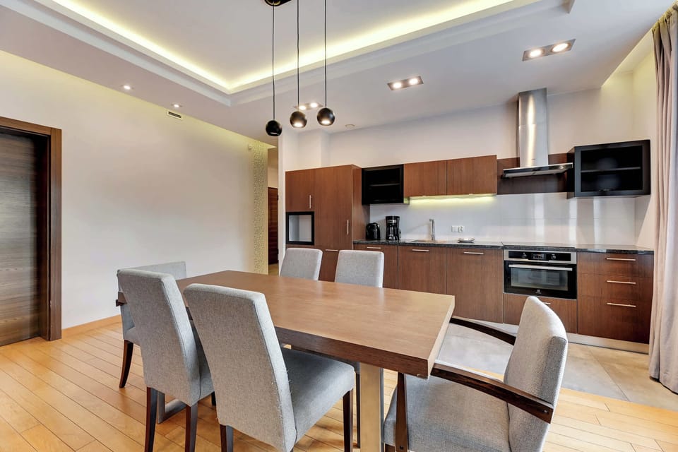 A spacious dining setup with a wooden table and upholstered chairs, surrounded by natural light from large windows.
