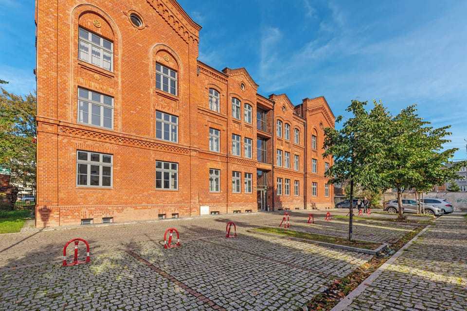 A picturesque scene showing a classic brick building with a cobblestone street and greenery, capturing the charm of the area.
