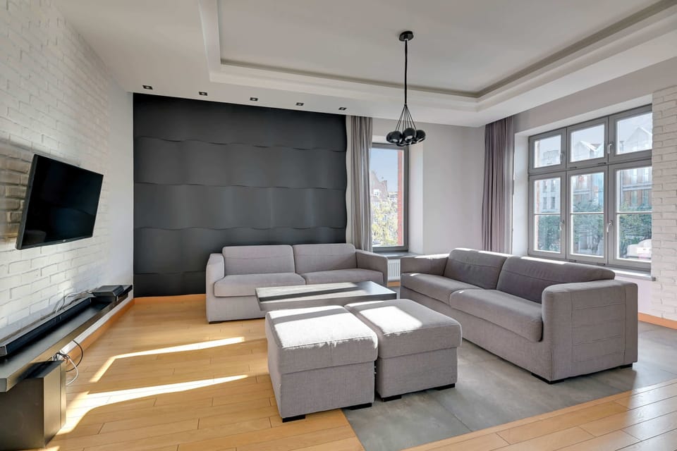 A modern living room with a sectional sofa, a flat-screen TV, and warm wooden floors complemented by soft lighting.