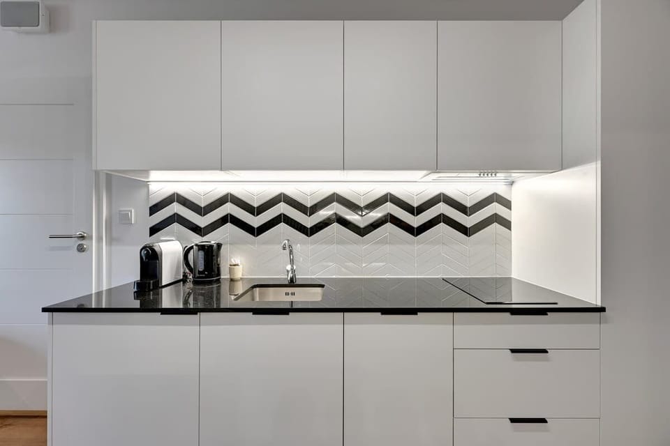 A modern kitchenette in contrasting shades of white and black, distinguished by a geometric pattern on the wall and a minimalist design.