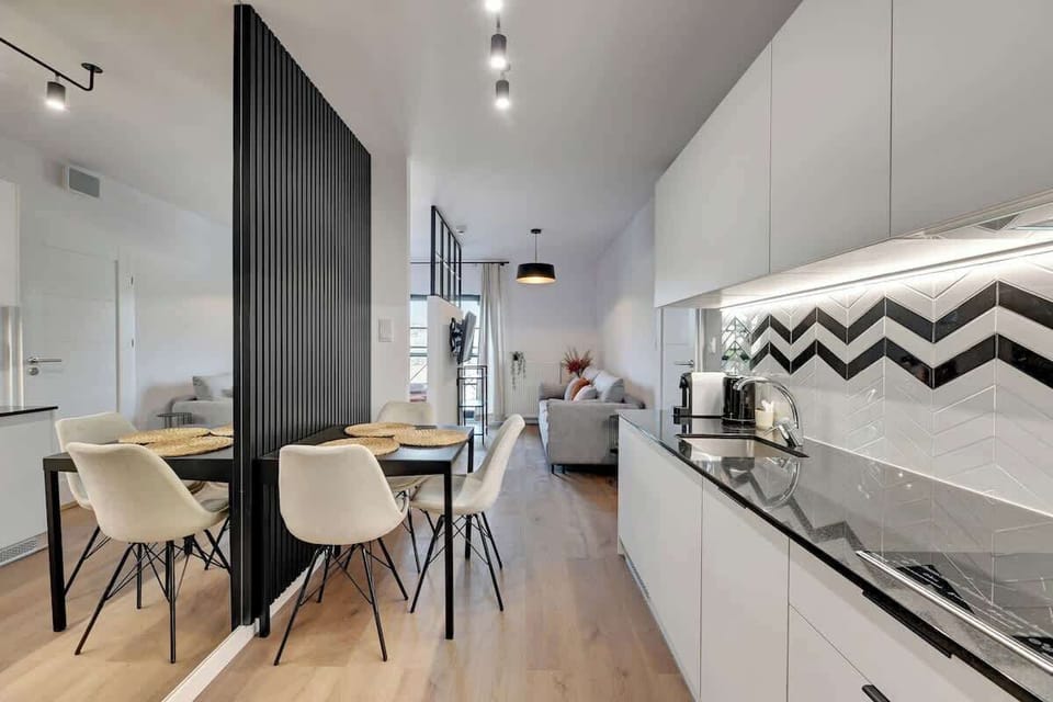 The modern interior combines a contrasting kitchenette, a minimalist dining table and a bright living room in the background.

