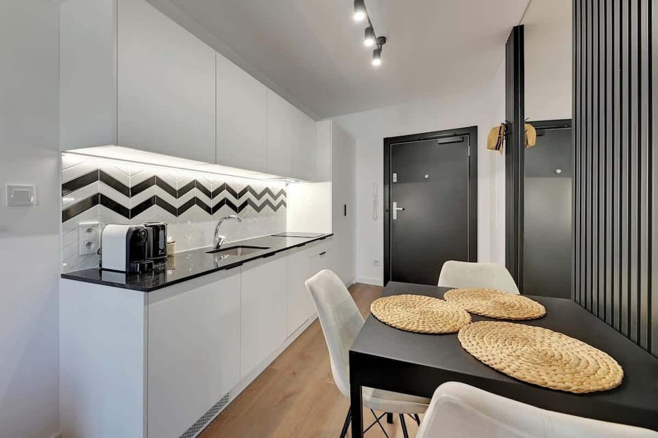 An elegant kitchenette with white furniture and a black and white pattern on the wall is complemented by a minimalist dining table with natural placemats.