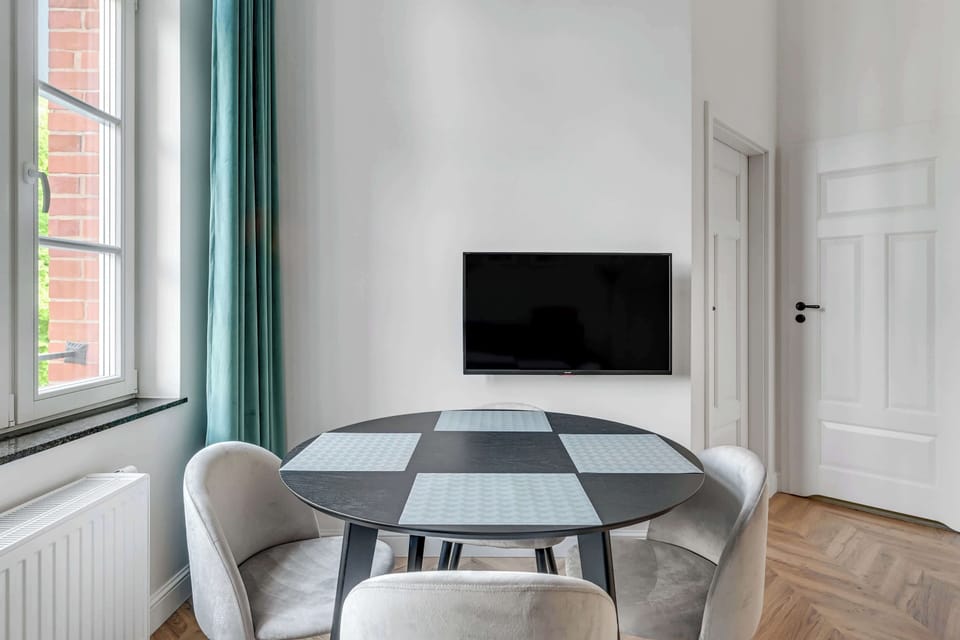 A bright and modern living room with a round dining table, elegant green chairs, and a plant adding a fresh touch to the decor.